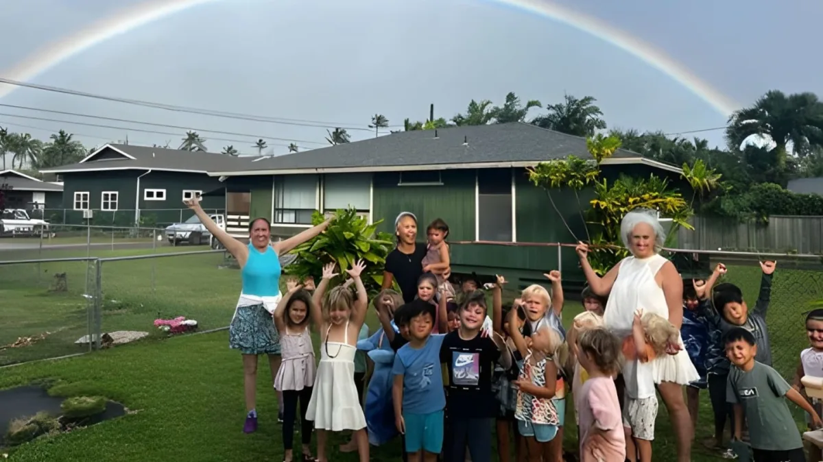 Aloha School keiki and teachers cheering under a rainbow outside the school